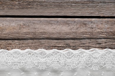 Photo of White lace on wooden table, top view. Space for text