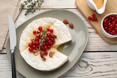 Photo of Brie cheese served with almonds, red currants and honey on white wooden table, flat lay