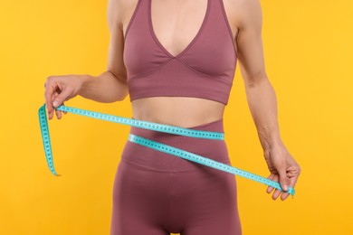 Photo of Slim woman measuring waist with tape on yellow background, closeup. Weight loss
