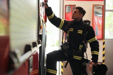 Firefighter in uniform opening door of fire truck at station