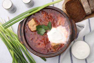 Tasty borscht with sour cream in bowl served with green onion on light grey table, flat lay