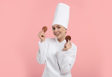 Happy professional confectioner in uniform holding delicious macarons on pink background