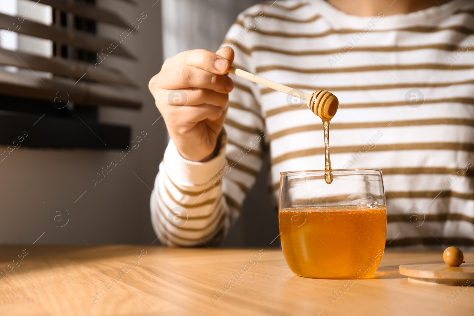 Photo of Woman with honey and dipper at wooden table, closeup