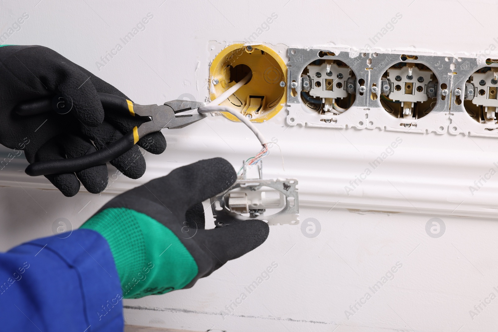 Photo of Professional repairman fixing power sockets with pliers indoors, closeup