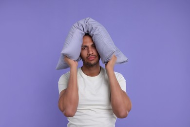 Photo of Tired man covering ears with pillow on violet background. Insomnia problem