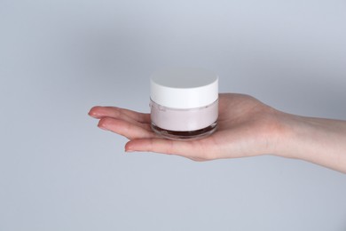 Woman holding jar of cream on grey background, closeup