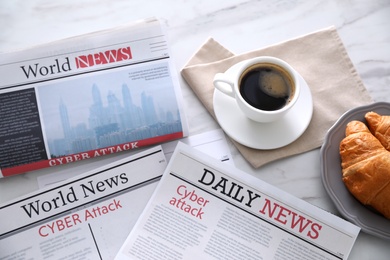 Photo of Newspapers with headlines CYBER ATTACK, coffee and croissant on white table