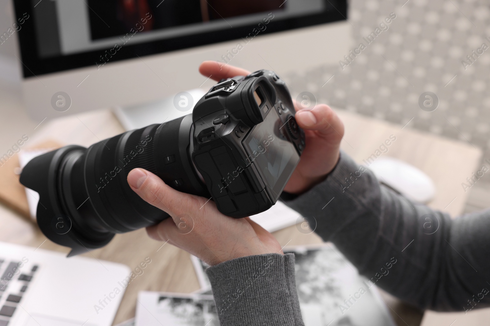 Photo of Professional photographer with digital camera at table indoors, closeup