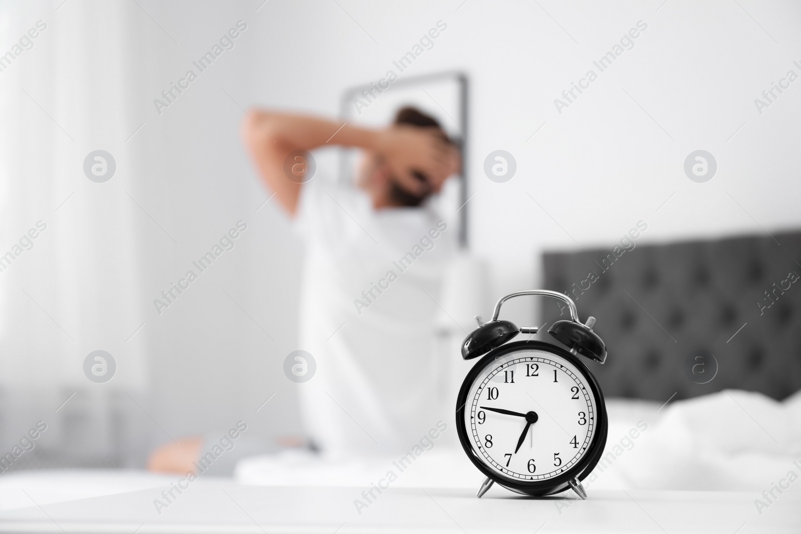 Photo of Analog alarm clock and blurred man on background. Time of day