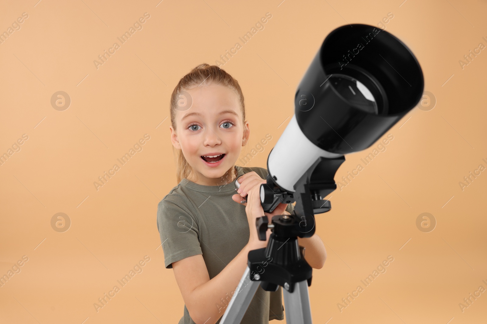 Photo of Surprised little girl with telescope on beige background