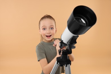 Surprised little girl with telescope on beige background