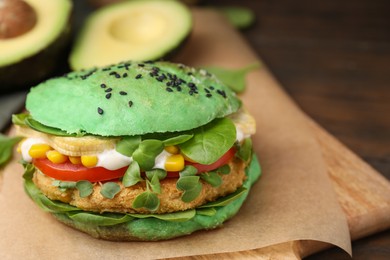 Photo of Tasty green vegan burger with vegetables, patty and microgreens on wooden table, closeup. Space for text