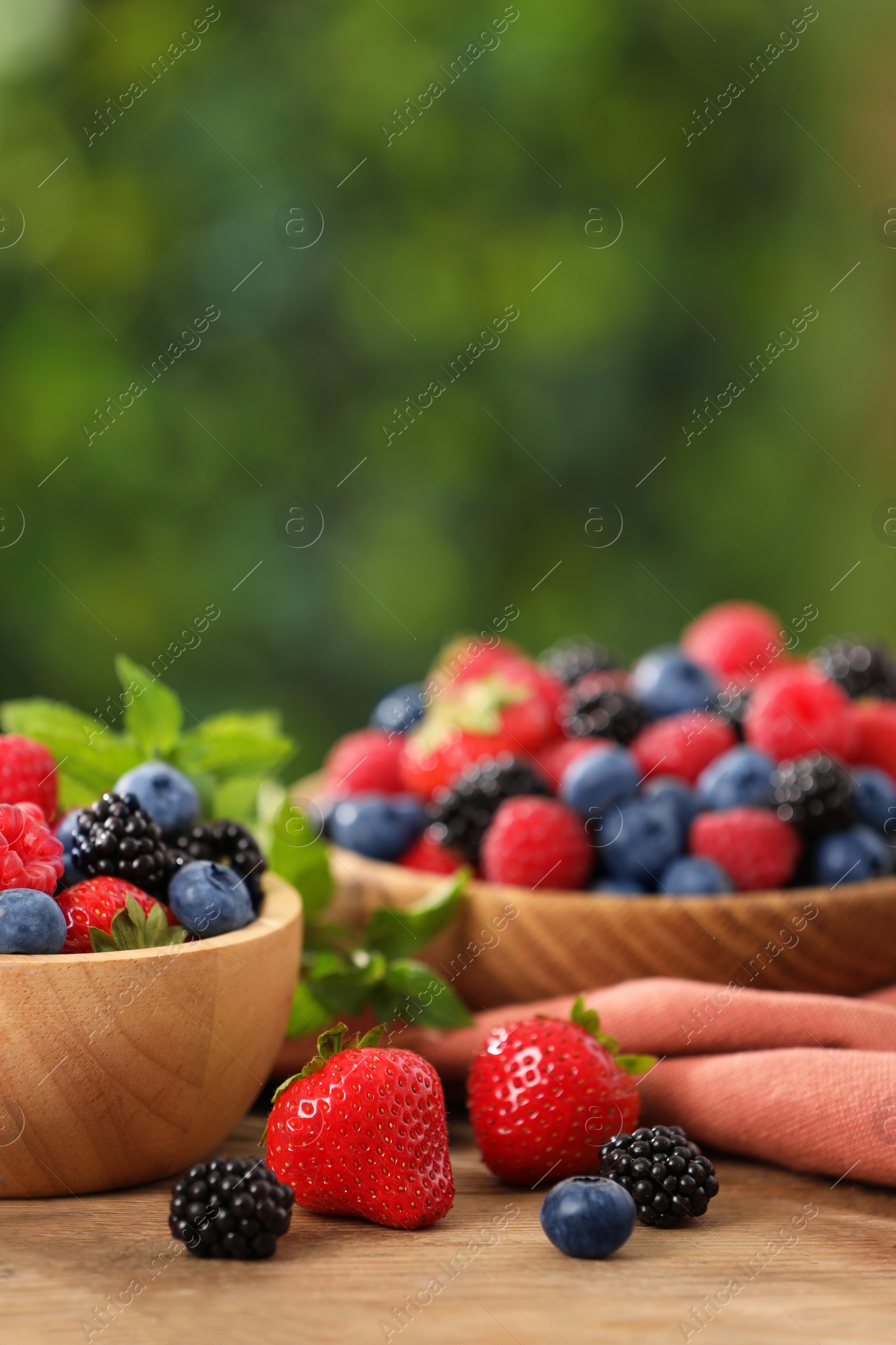 Photo of Bowls with different fresh ripe berries and mint on wooden table outdoors