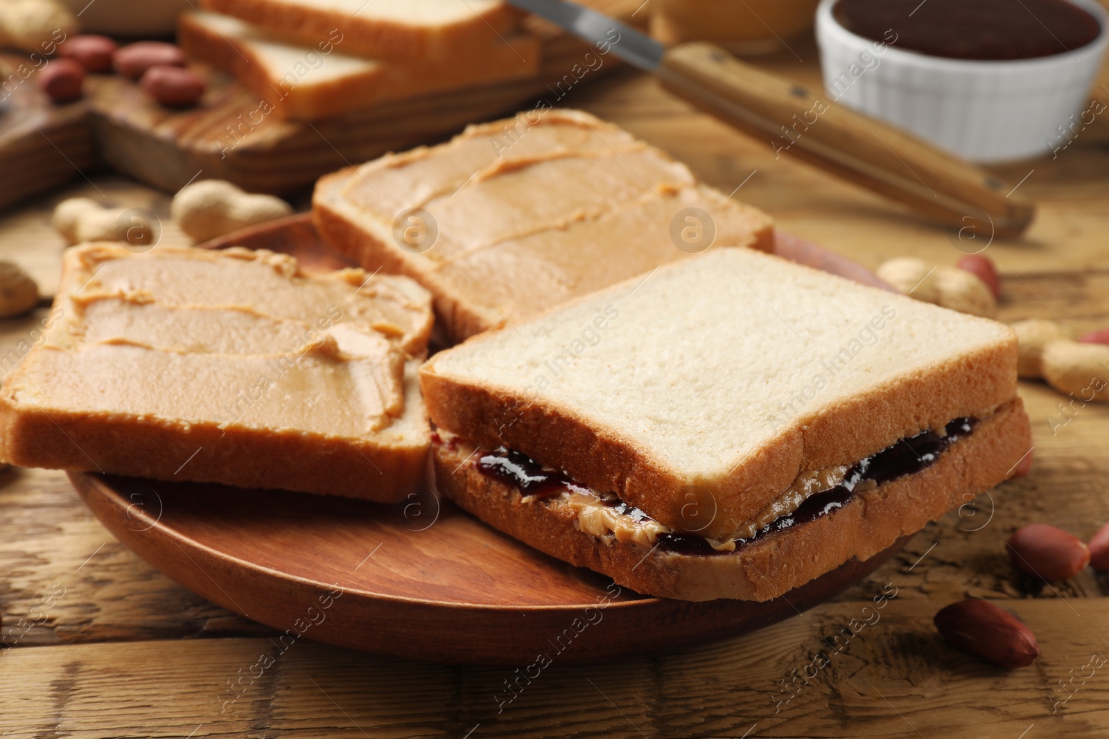 Photo of Tasty peanut butter sandwiches with jam and peanuts on wooden table, closeup