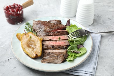Photo of Delicious roasted beef meat, caramelized pear and greens served on light textured table
