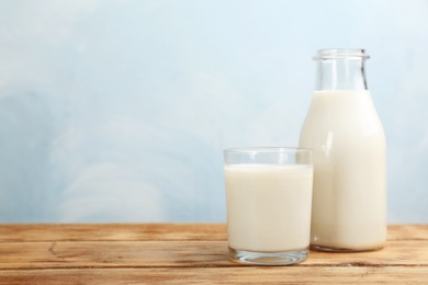 Photo of Glass and bottle with fresh milk on table against color background. Space for text