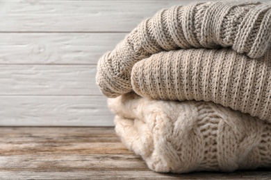 Photo of Stack of folded knitted sweaters on table. Space for text