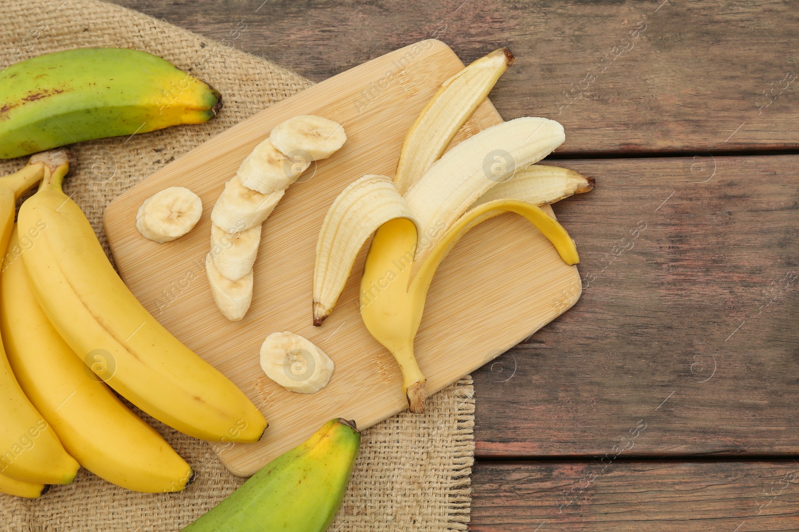 Photo of Whole and cut bananas on wooden table, flat lay. Space for text