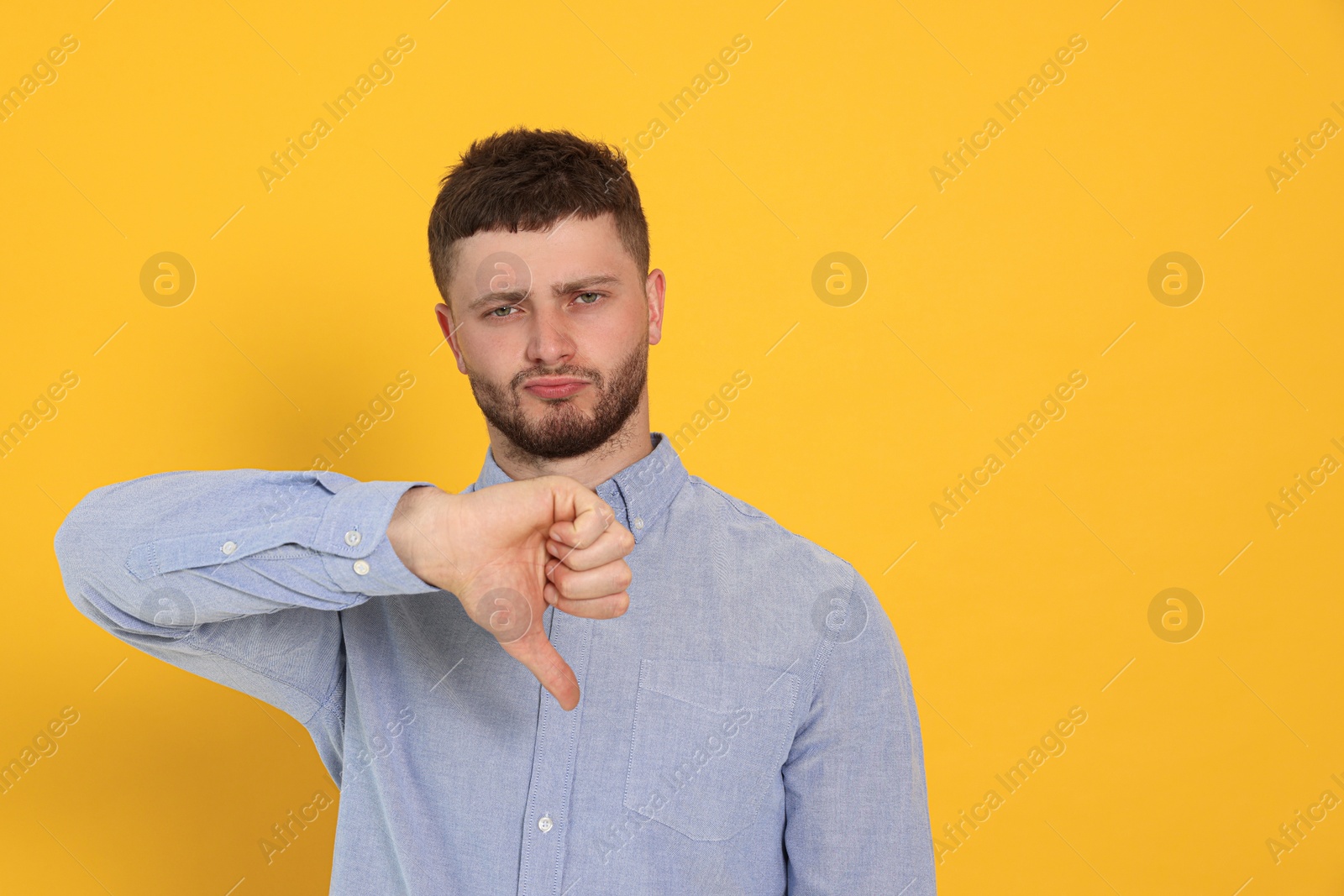 Photo of Young man showing thumb down on orange background, space for text