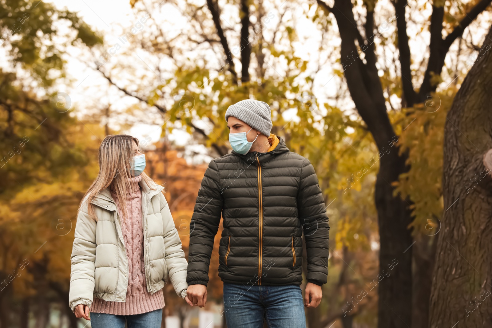 Photo of Couple in medical masks walking outdoors on autumn day. Protective measures during coronavirus quarantine