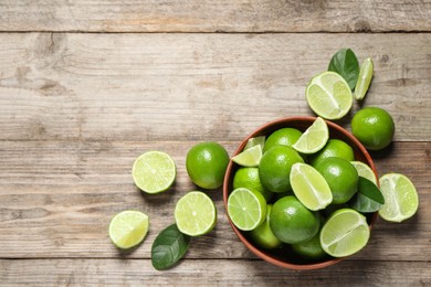Photo of Tasty ripe limes in bowl on wooden table, top view. Space for text