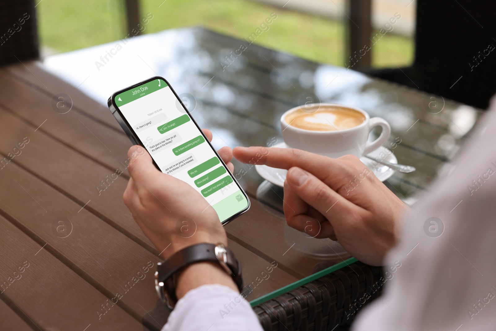 Image of Man texting via mobile phone at table outdoors, closeup. Device screen with messages