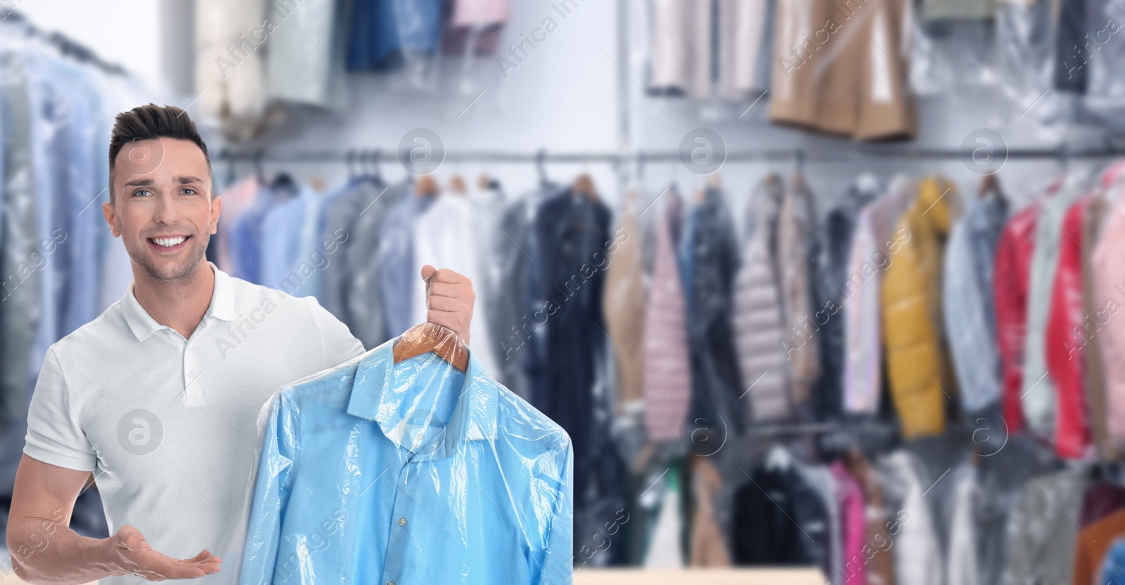 Image of Dry-cleaning service. Happy man holding hanger with shirt in plastic bag indoors, space for text. Banner design