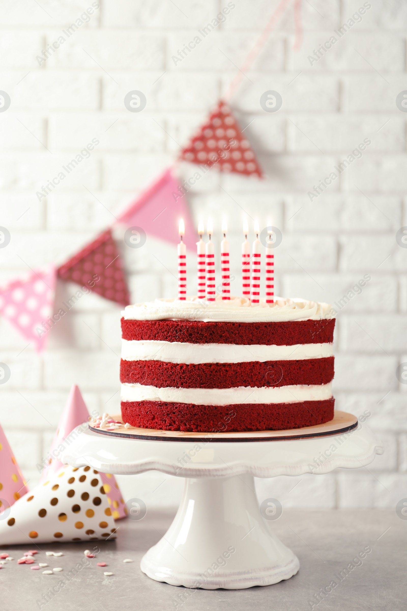 Photo of Delicious homemade red velvet cake with candles on table against brick wall