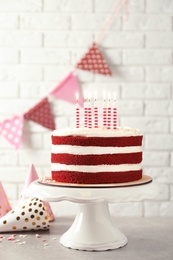 Photo of Delicious homemade red velvet cake with candles on table against brick wall