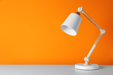 Stylish modern desk lamp on white table near orange wall, space for text