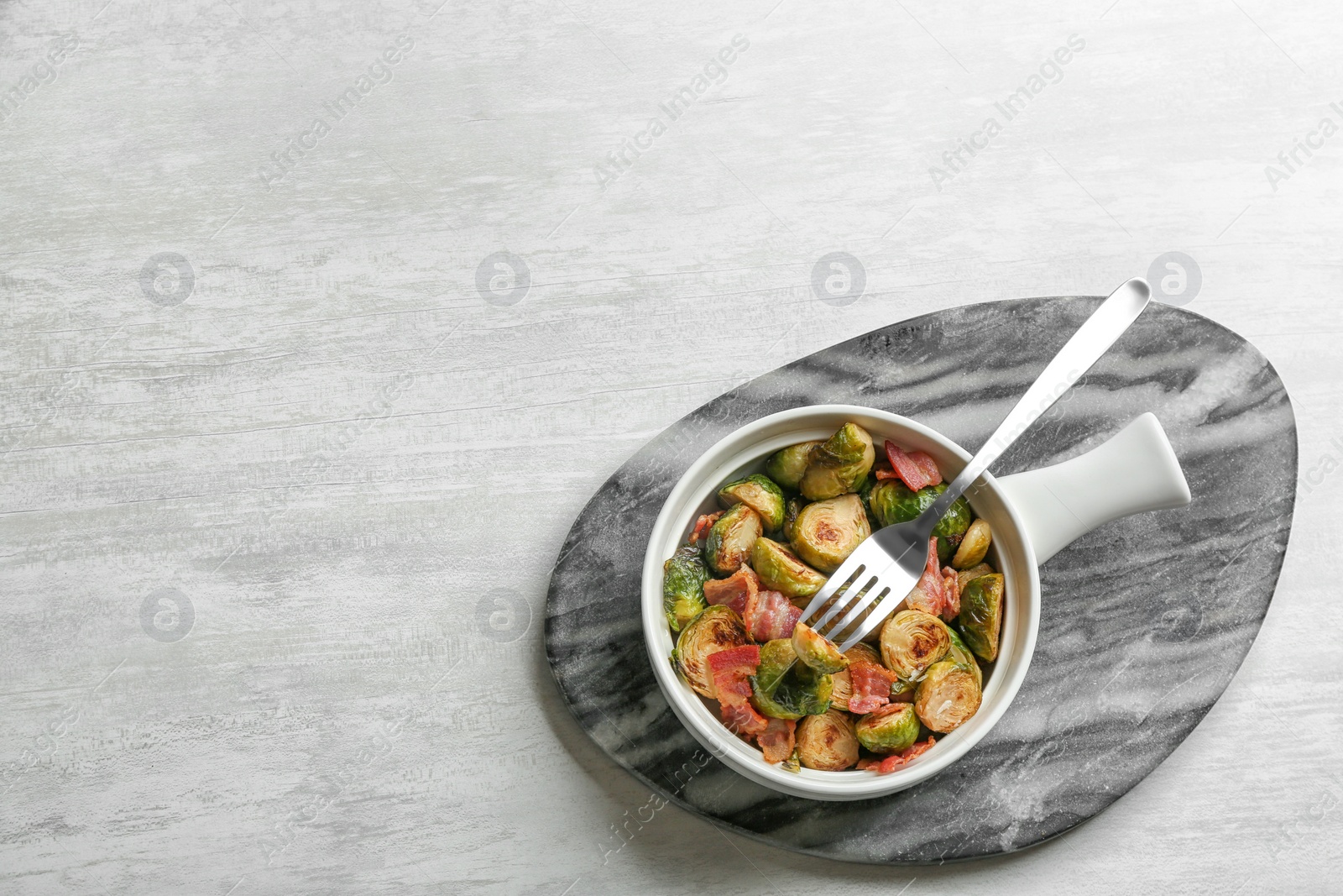 Photo of Roasted Brussels sprouts with bacon served on white wooden table, top view. Space for text