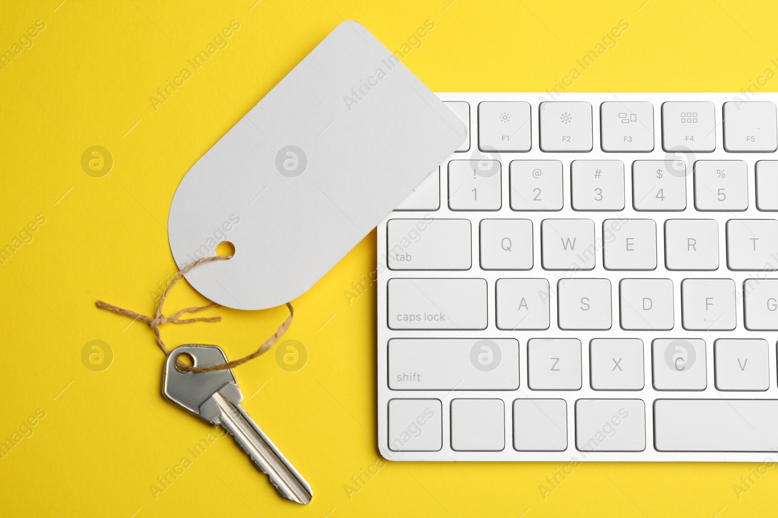 Photo of Key with blank tag and keyboard on yellow background, flat lay. Keyword concept