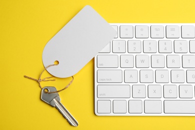 Key with blank tag and keyboard on yellow background, flat lay. Keyword concept