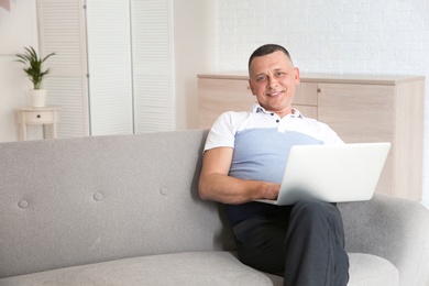 Photo of Mature man with laptop sitting on sofa at home