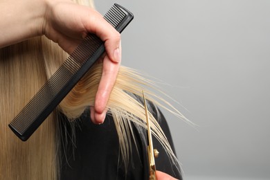 Hairdresser cutting client's hair with scissors on light grey background, closeup. Space for text