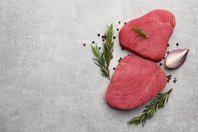 Fresh raw tuna fillets with rosemary and spices on light gray table, flat lay. Space for text