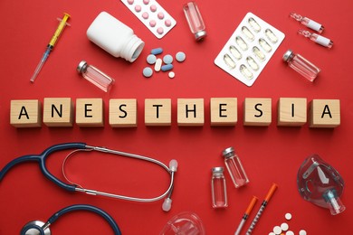 Word Anesthesia made of wooden cubes, stethoscope and drugs on red background, flat lay