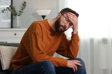 Photo of Overwhelmed man in glasses sitting on sofa at home