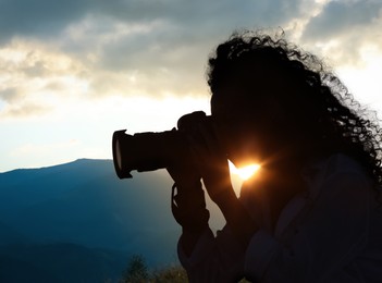 Photographer taking picture of beautiful mountains at sunset with professional camera