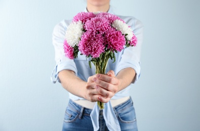 Photo of Woman with bouquet of beautiful asters on light background, closeup. Autumn flowers