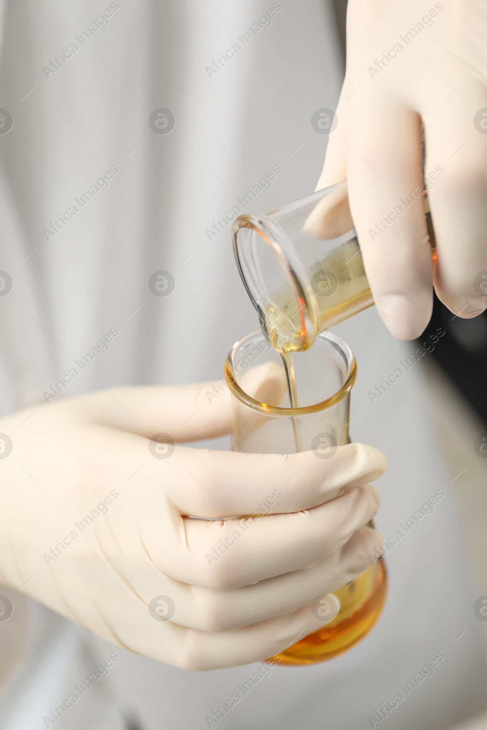 Photo of Laboratory worker pouring orange crude oil into flask, closeup