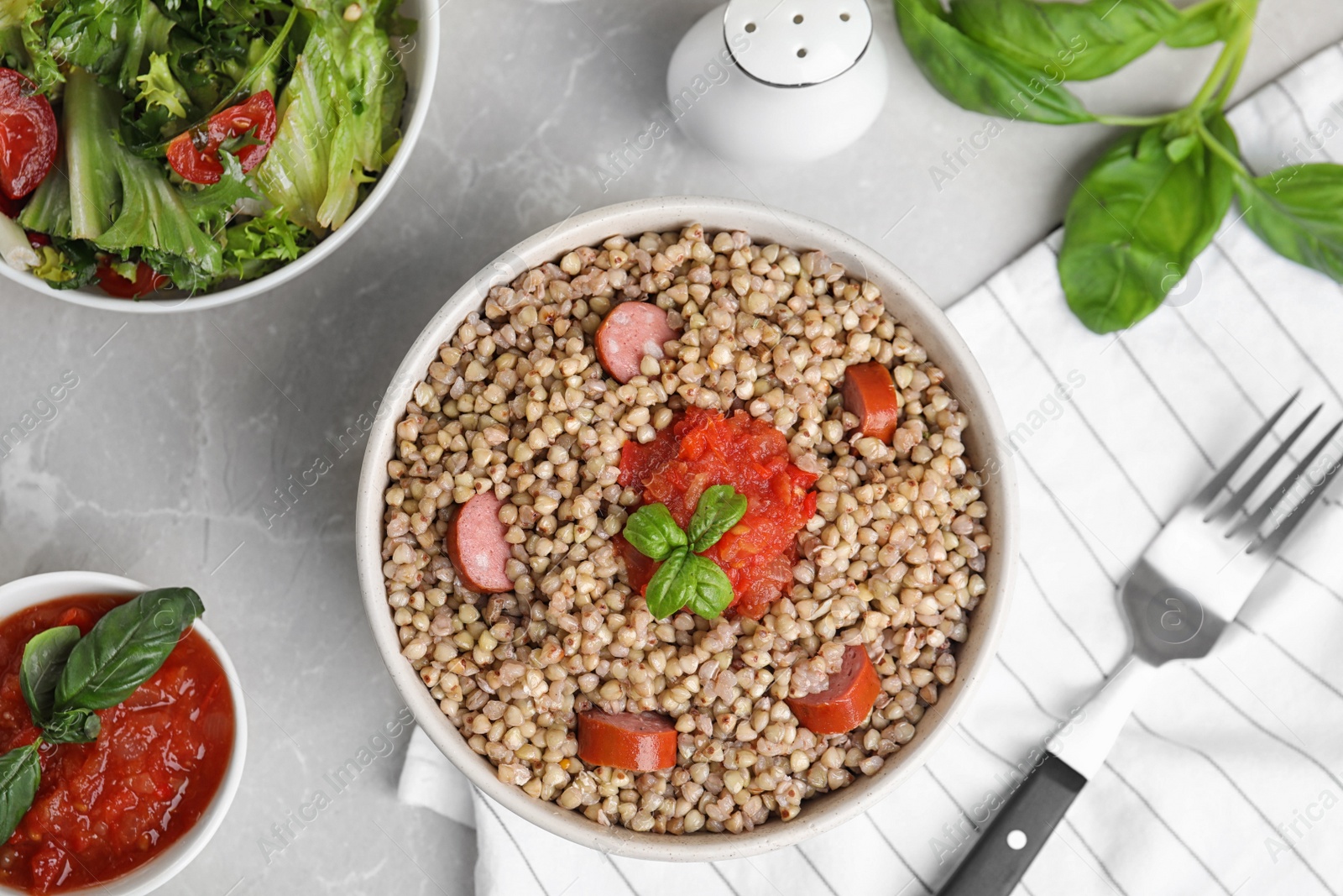 Photo of Tasty buckwheat porridge with sausages on grey marble table, flat lay