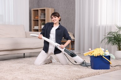 Photo of Happy young housewife vacuuming carpet at home