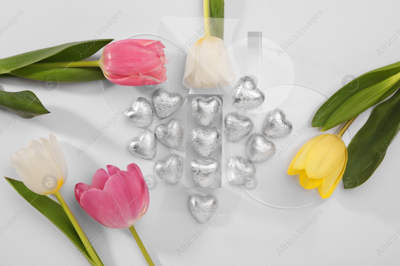 Photo of Heart made with delicious chocolate candies and beautiful tulips on white background, top view