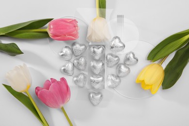 Photo of Heart made with delicious chocolate candies and beautiful tulips on white background, top view