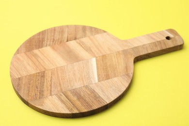 Photo of One wooden cutting board on yellow background, closeup. Cooking utensil