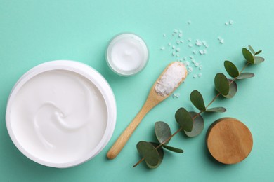 Moisturizing cream in open jars, sea salt and eucalyptus branch on turquoise background, flat lay. Body care products