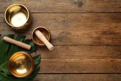 Photo of Golden singing bowls, mallets and monstera leaf on wooden table, flat lay. Space for text