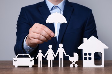 Photo of Man holding figure of umbrella above family at wooden table. closeup. Insurance concept