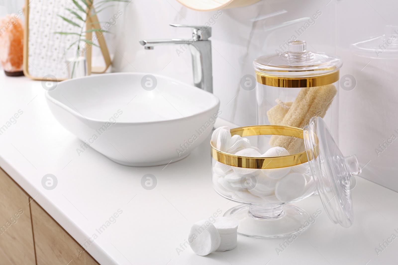 Photo of Glass jars with cotton pads and loofahs on table in bathroom